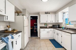 Una cocina moderna con armarios blancos, un microondas, un lavabo y una cortina roja al fondo.