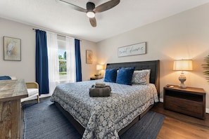 A bedroom with a bed, a nightstand, a lamp, a ceiling fan, and a window with curtains. - ⚓Sunset Getaways! Private Heated Pool home, Cinema/Arcade Room⚓ (Bradenton)