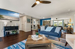 A modern living room with a blue sofa, wooden coffee table, and a ceiling fan. - ⚓Sunset Getaways! Private Heated Pool home, Cinema/Arcade Room⚓ (Bradenton)