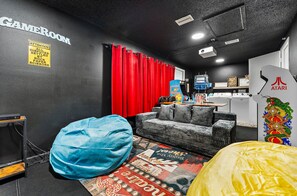 Habitación con zona de juegos, sofá, pufs, espacio para lavandería y una pared con un letrero de advertencia.