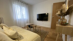 Een moderne slaapkamer met een groot bed, een tv aan de muur, een klein rond tafeltje en een houten deur.