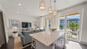 A modern kitchen with a large island, a grey sofa, and a flat-screen TV.