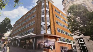 Un edificio de varios pisos con entrada en esquina, amplias ventanas y locales comerciales en la planta baja.