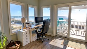 Ein Zimmer mit Schreibtisch, Stuhl und großen Fenstern mit Blick auf den Strand.