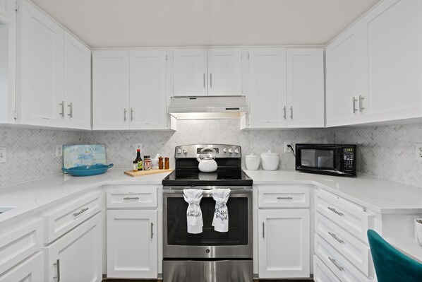 A modern kitchen with white cabinets, stainless steel appliances, and a herringbone tile backsplash.