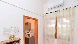 A small, clean room with a microwave on a counter, a wooden shelf with papers, and a curtain with a floral pattern. - Holiday apartment with air conditioning (Pula)