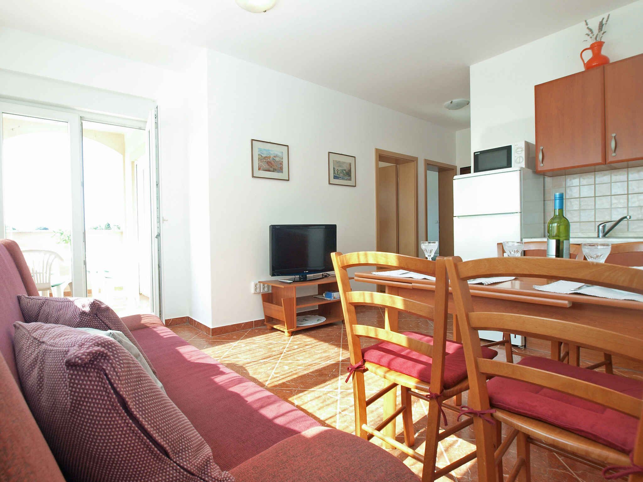 Ein Wohnzimmer mit einer Couch, Holzstühlen, einem Fernseher und einer Küchenzeile mit Schränken und einer Weinflasche.