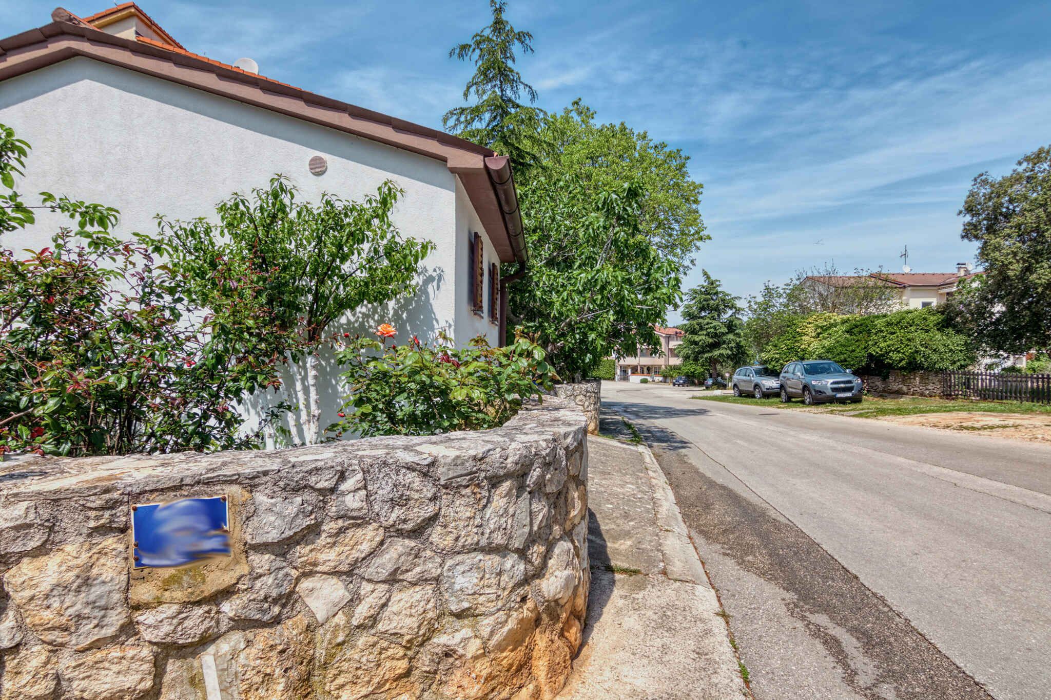 A stone wall with a blue sign, a white building with a brown roof, and parked cars on a street.