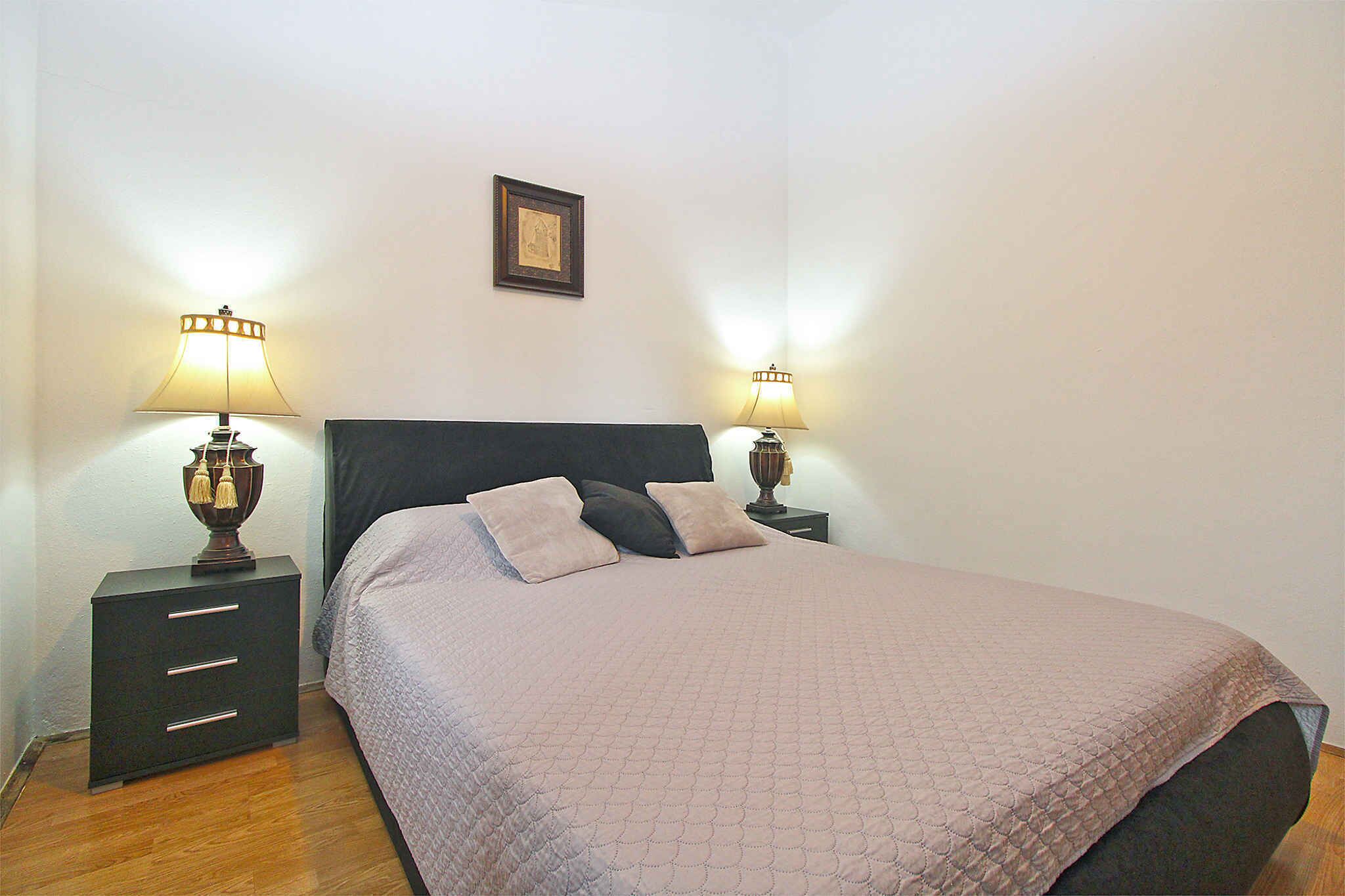 A neatly made bed with a quilted cover, two bedside tables with lamps, and a framed picture on the wall.