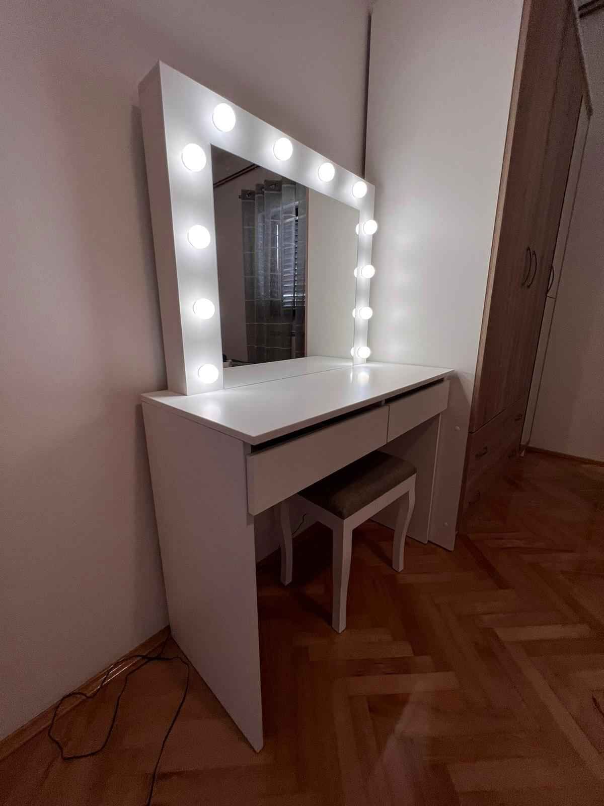 A white vanity with a mirror and lights, a bench, and a wooden floor.