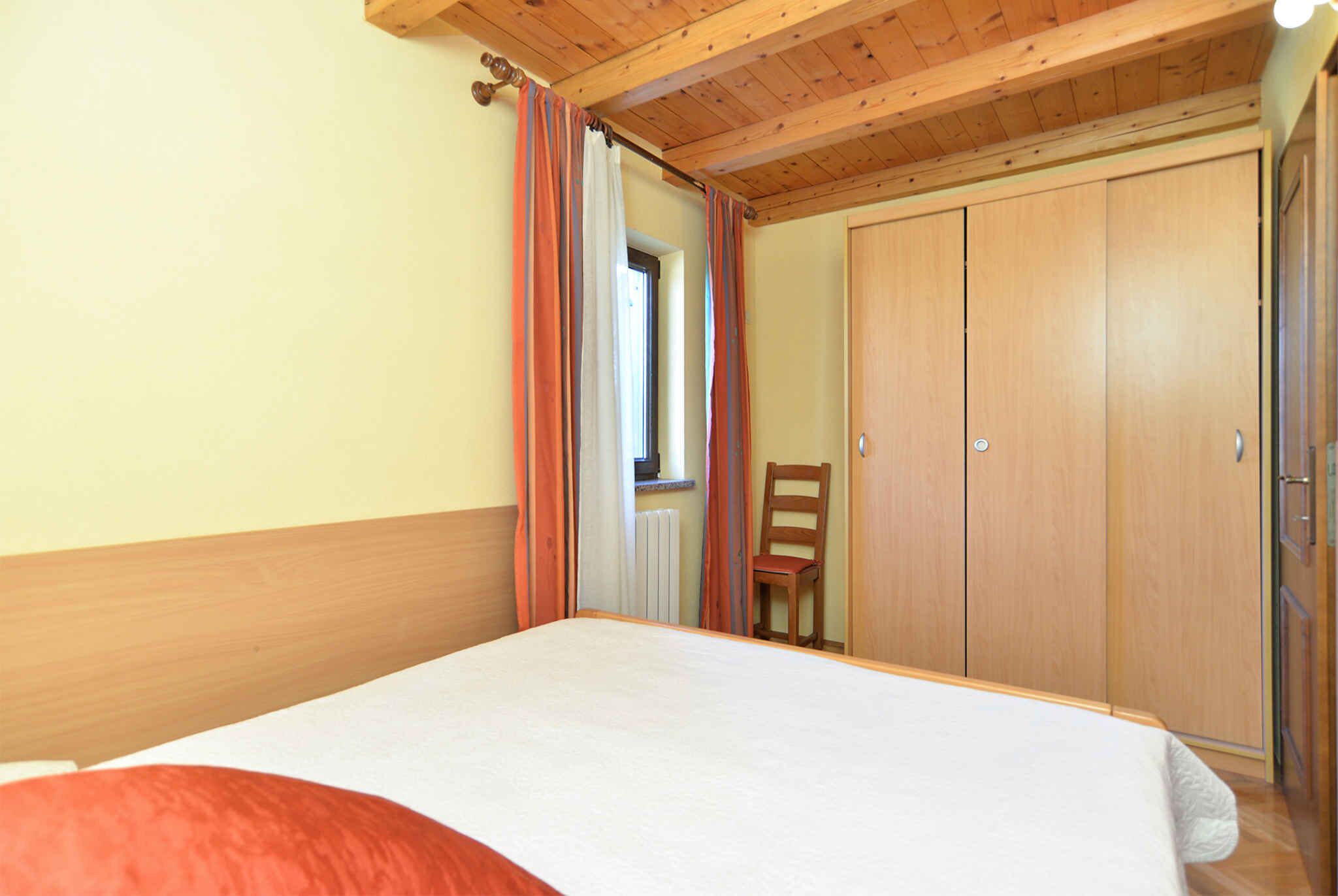 A bedroom with a bed, wooden wardrobe, and a chair.