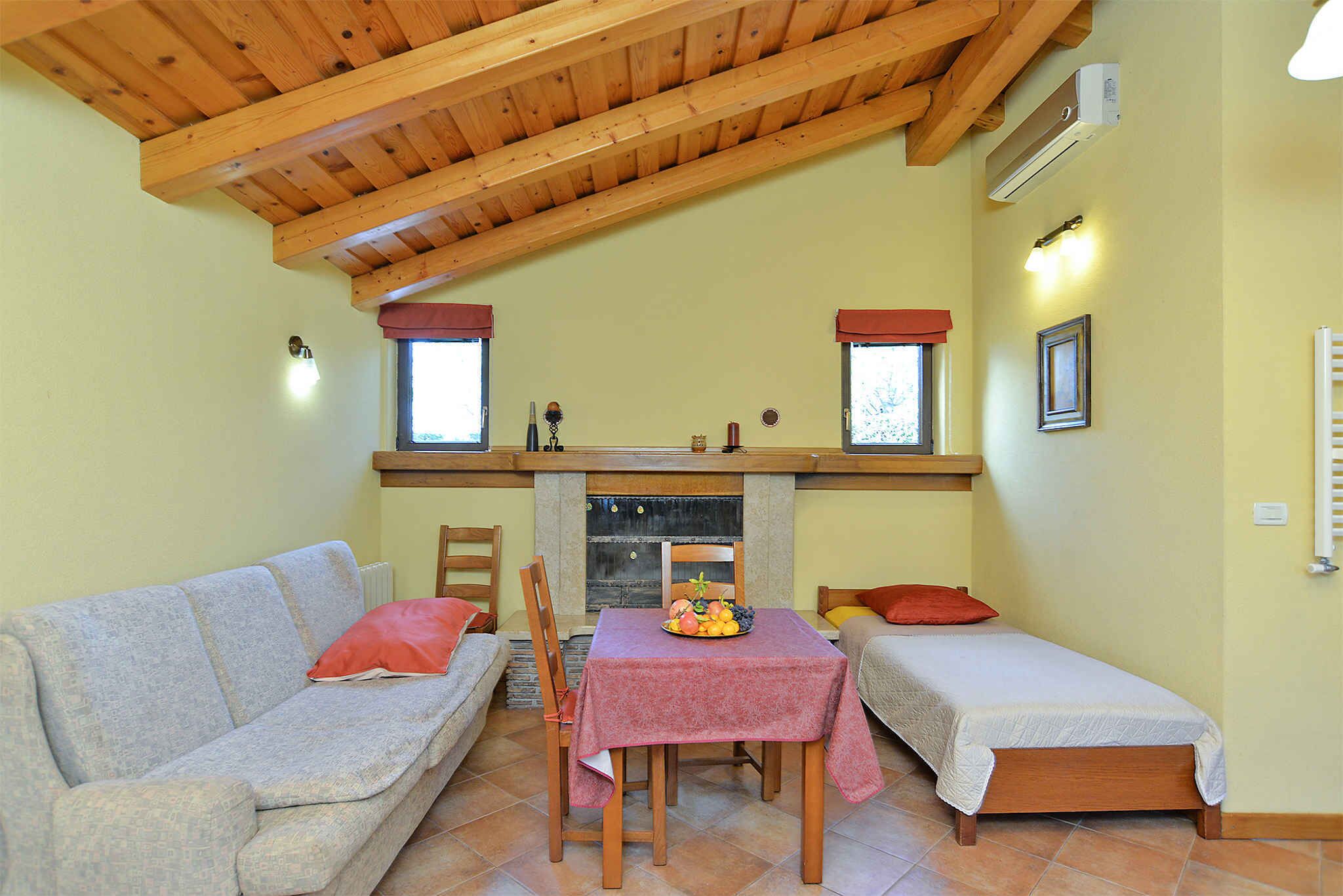 Una stanza accogliente con soffitto in legno, un camino, un tavolo da pranzo con una ciotola di frutta, due letti e un divano.