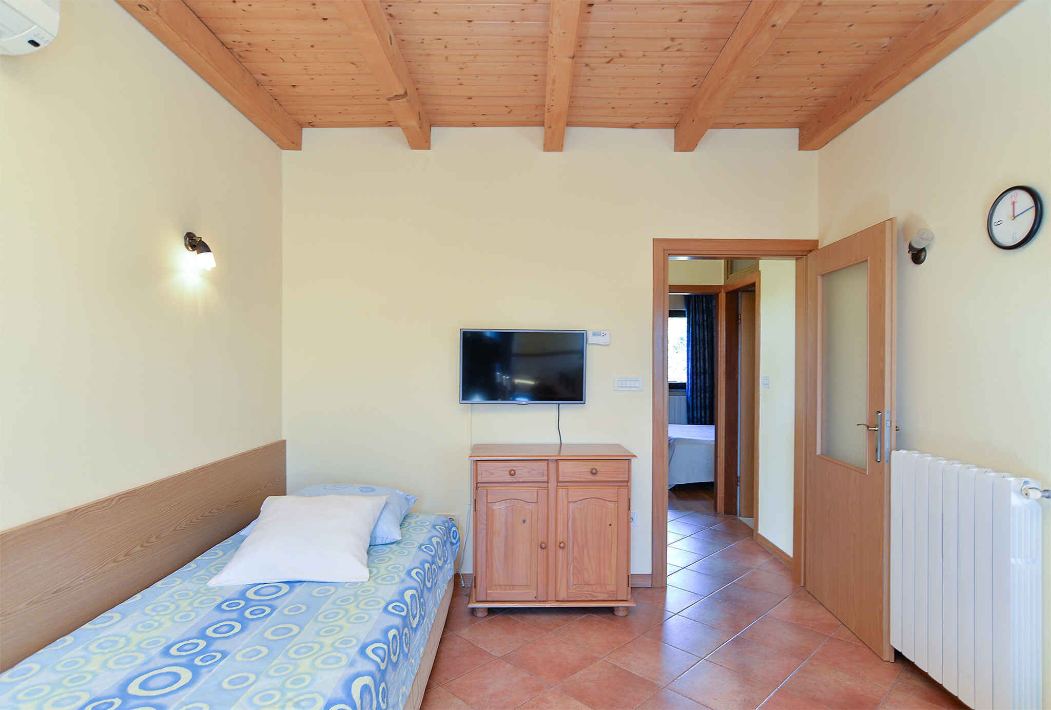 Ein Schlafzimmer mit Bett, Holzschrank, Fernseher, einer Uhr und einer Heizung.