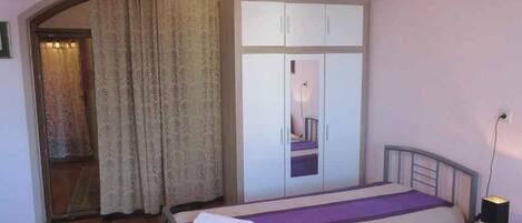 A bedroom with a bed, a wardrobe, a nightstand, and a lamp.