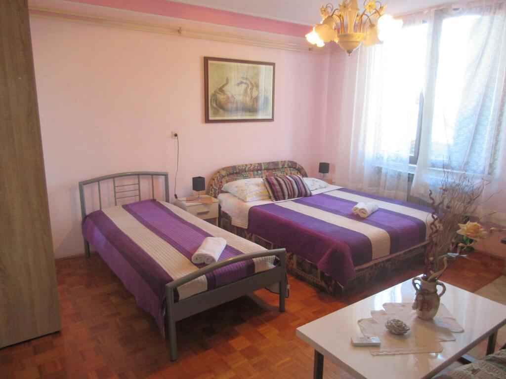 Quarto com duas camas, piso de madeira, um quadro na parede, um candelabro e uma janela com cortinas.