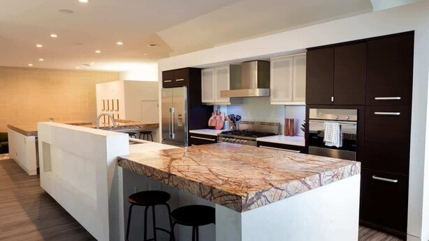 A modern kitchen with dark cabinetry, a marble island, and a stainless steel range hood. - Rice Village Retreat - Rooftop deck & BBQ grill (Houston)