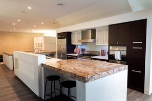 Una cocina moderna con armarios oscuros, una isla de mármol y una campana extractora de acero inoxidable.