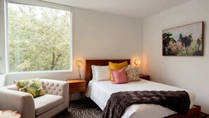 A bedroom with a bed, a nightstand, a chair, a window with a view of trees, and a painting on the wall. - Rice Village Retreat - Rooftop deck & BBQ grill (Houston)