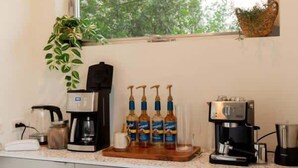 A kitchen with a coffee station, a window with a view of trees, and a shelf with mugs. - Rice Village Retreat - Rooftop deck & BBQ grill (Houston)