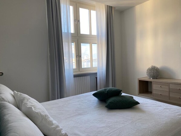 Ein Schlafzimmer mit einem Bett, zwei Kissen, einer Kommode und einem Fenster mit Vorhängen.