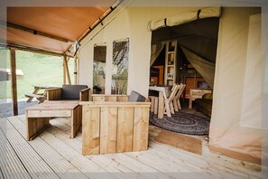 Une terrasse en bois avec une table et des chaises, un espace salon couvert et une pièce sous tente équipée d’un lit et d’une petite table.