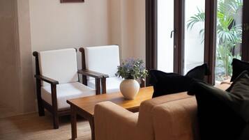 Una habitación con dos sillas blancas, una mesa de madera con un florero y un sofá color crema.