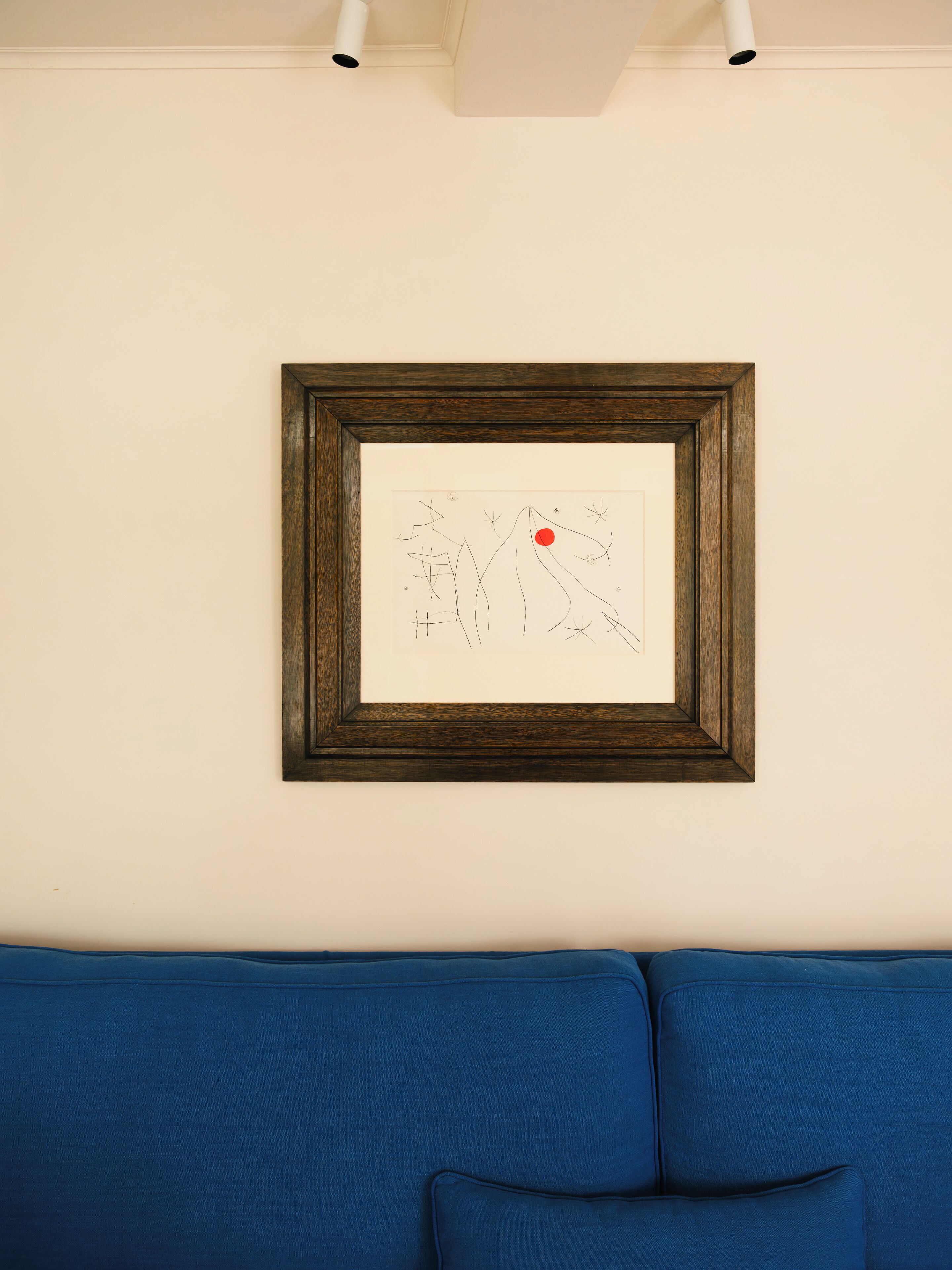 A framed abstract artwork on a white wall above a blue sofa.