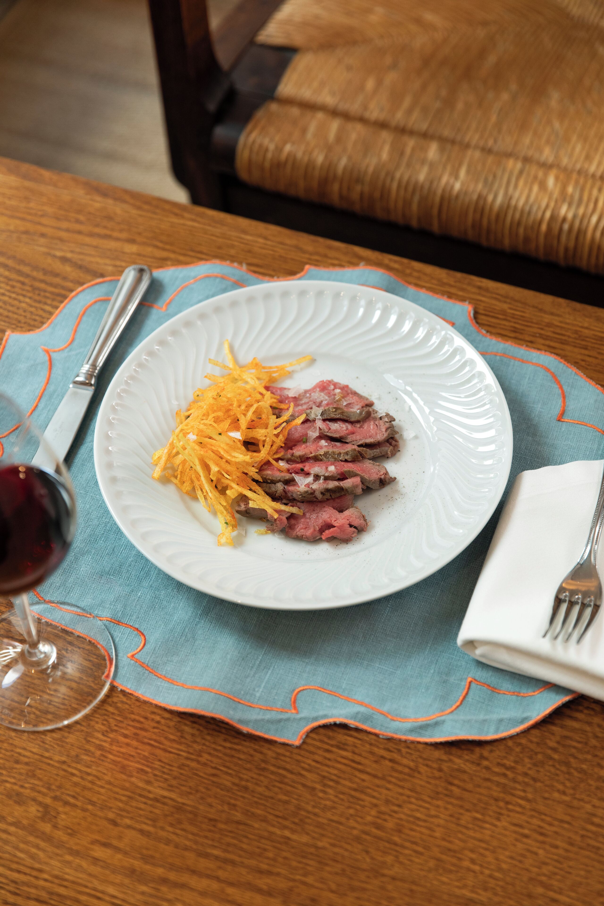 Un plato de carne en rodajas con queso rallado, sobre un plato blanco, colocado sobre una mesa con un mantel individual azul.