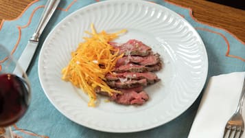 Un plato de carne en rodajas con queso rallado, sobre un plato blanco, colocado sobre una mesa con un mantel individual azul.