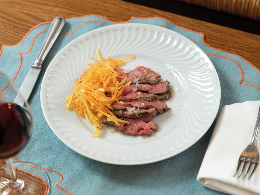 Un plato de carne en rodajas con queso rallado, sobre un plato blanco, colocado sobre una mesa con un mantel individual azul.