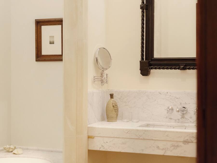 Un baño con lavamanos de mármol, un taburete de madera, un cuadro en la pared y un espejo sobre el lavamanos.
