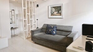 Una sala de estar moderna con un sofá gris, una mesita, un cuadro en la pared y una lámpara de techo blanca.
