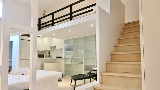 Una habitación de hotel moderna con una escalera de madera, una cama con ropa de cama blanca, una pequeña mesa y un armario con puertas de vidrio.