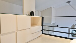 Una habitación moderna con separador de vidrio, armarios blancos y barandilla negra.