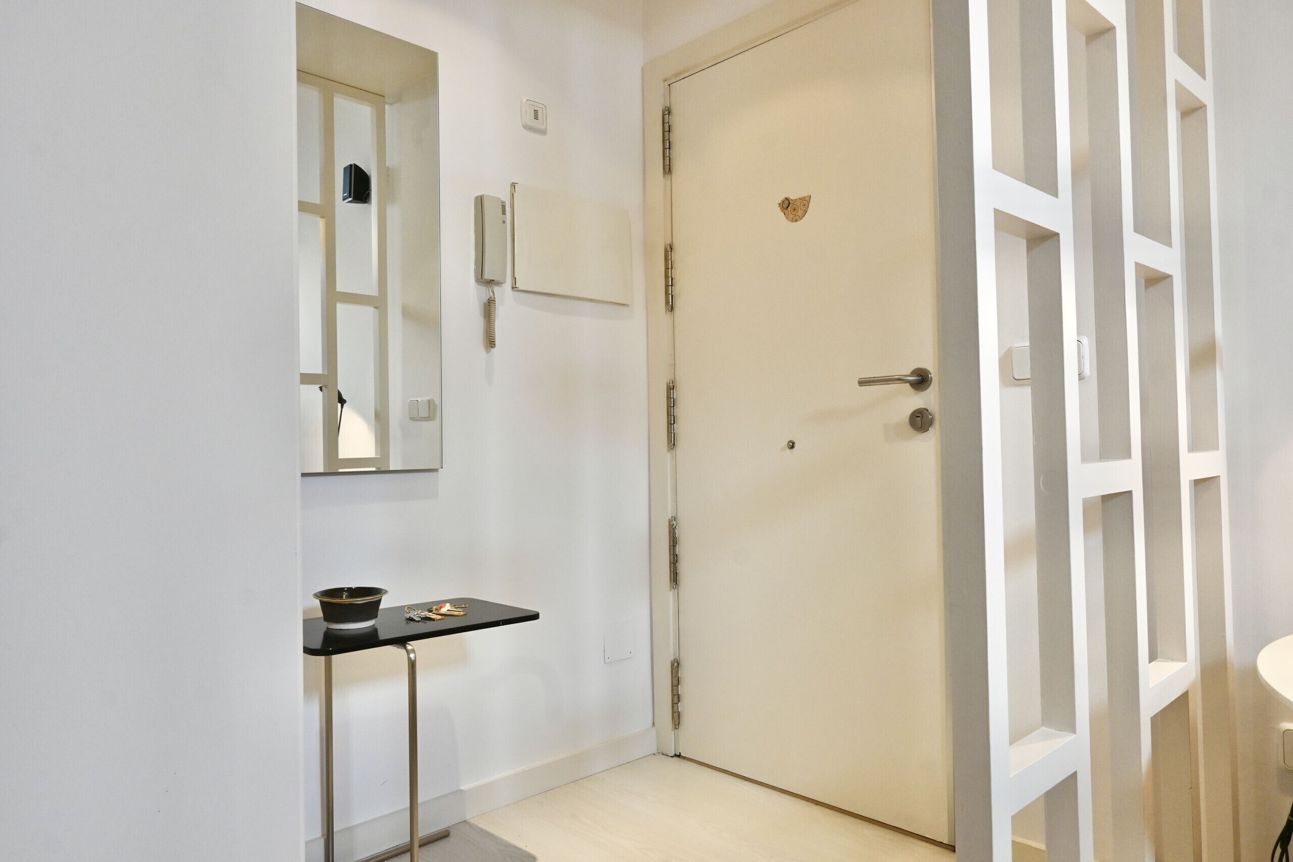 A hallway with a closed door, a small table with a bowl and keys, a mirror, and a wall-mounted phone.