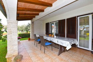 Relax in the serene patio area, surrounded by lush greenery and a brick wall, with a table for al fresco dining.