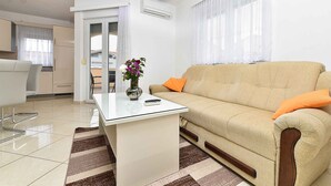 A modern living room with a beige sofa, a glass coffee table, and a dining area with a white table and chairs. - Holiday apartment with air conditioning (Medulin)