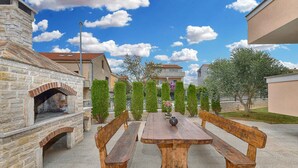 An outdoor patio with a stone fireplace, wooden benches, and a table with a vase. - Holiday apartment with air conditioning (Medulin)