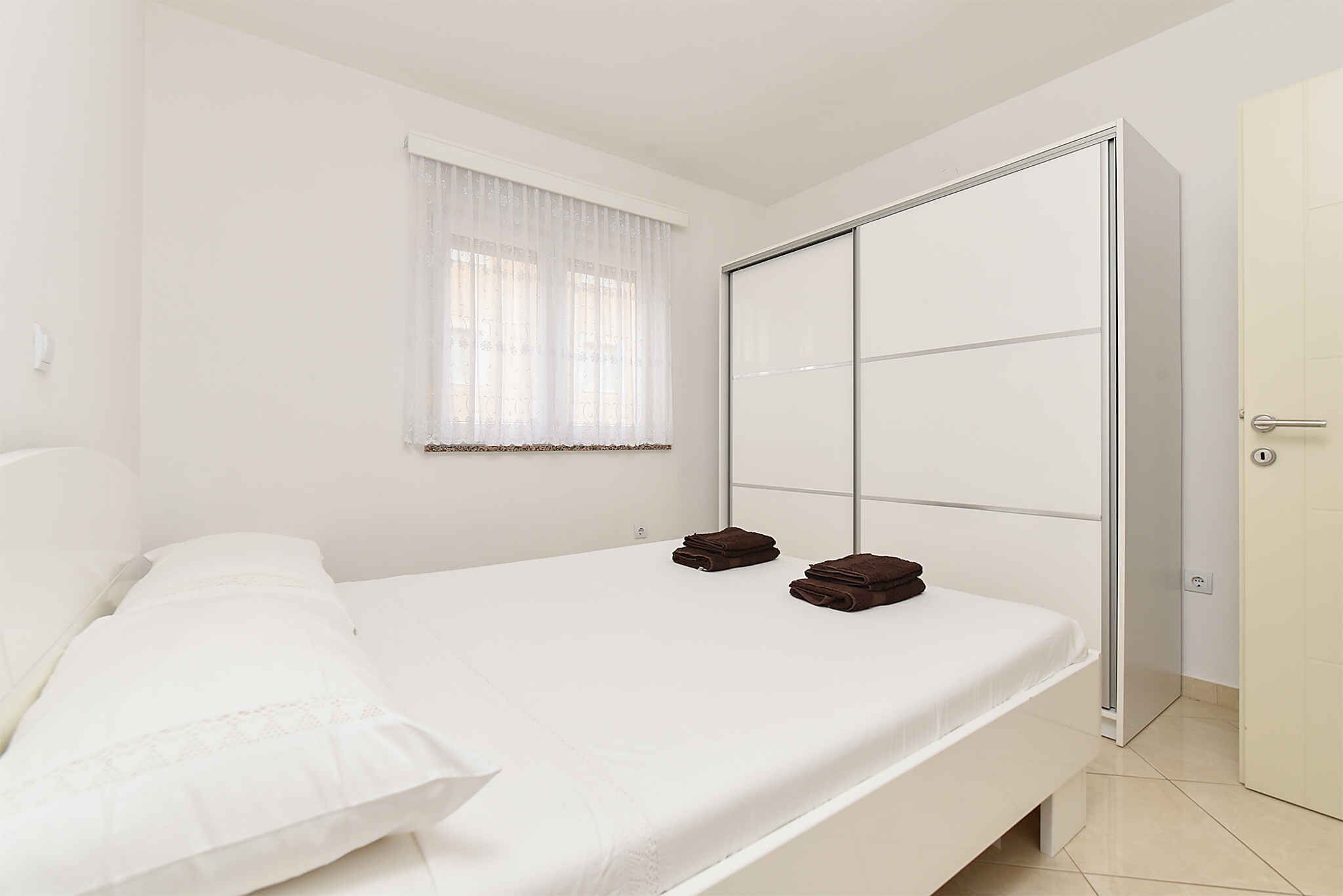 A bedroom with a bed, a wardrobe, and a window with sheer curtains.