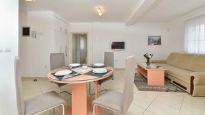 A modern living room with a round dining table, beige sofa, and a TV mounted on the wall. - Holiday apartment with air conditioning (Medulin)