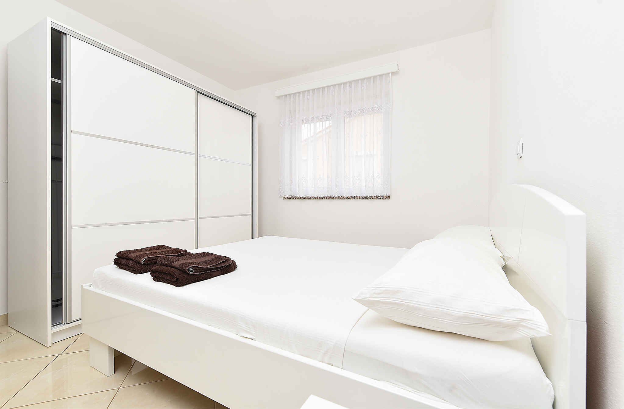 A bedroom with a bed, a wardrobe, and a window with sheer curtains.
