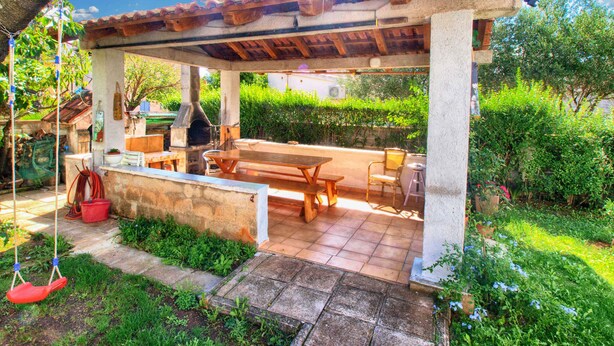 An outdoor patio with a wooden table and benches, a hanging swing, and a stone wall. - Holiday apartment with air conditioning (Medulin)