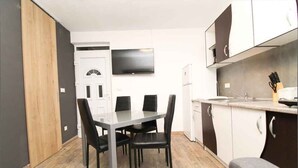 A compact kitchen with a dining table and chairs, a TV mounted above the counter, and a refrigerator.