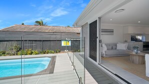 A modern house with a swimming pool, a glass door leading to a living area, and a wooden deck.