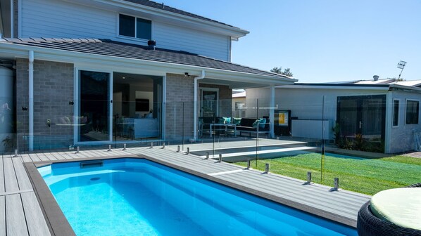 Una casa moderna con piscina, patio cubierto y jardín cercado.