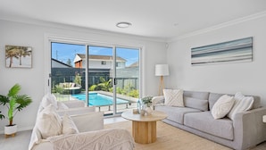 A modern living room with a pool view, a grey sofa, a round coffee table, and a large window.
