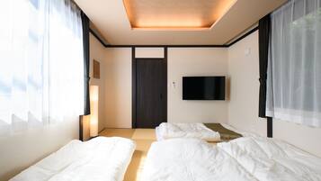 A hotel room with two beds, a flat-screen TV mounted on the wall, and a door in the center.