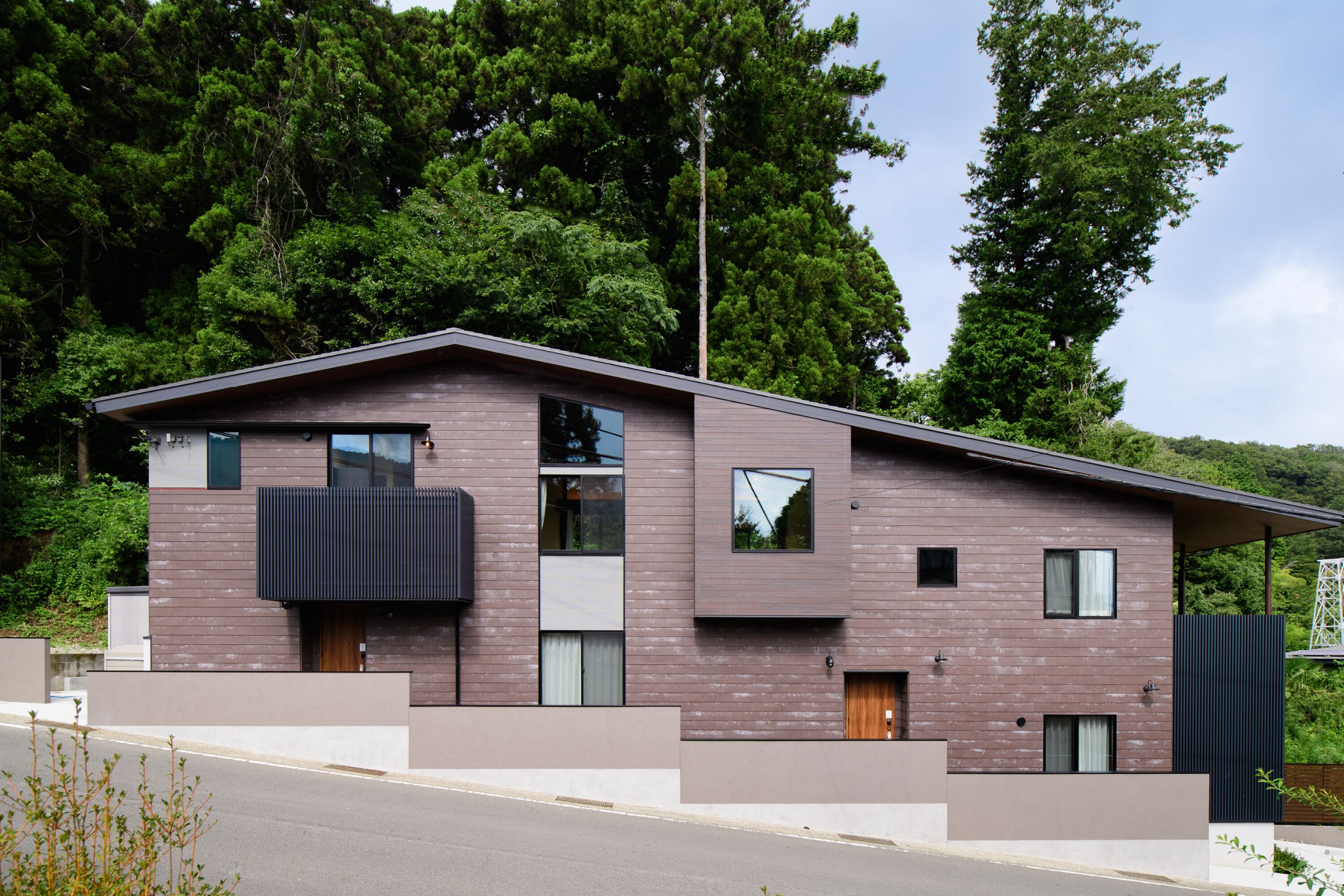 Une maison moderne à deux étages, dotée d’un toit plat, de grandes fenêtres et d’un balcon.