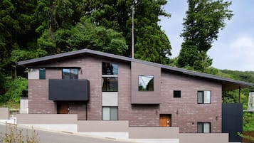 Una casa moderna de dos pisos con techo plano, ventanas grandes y un balcón.
