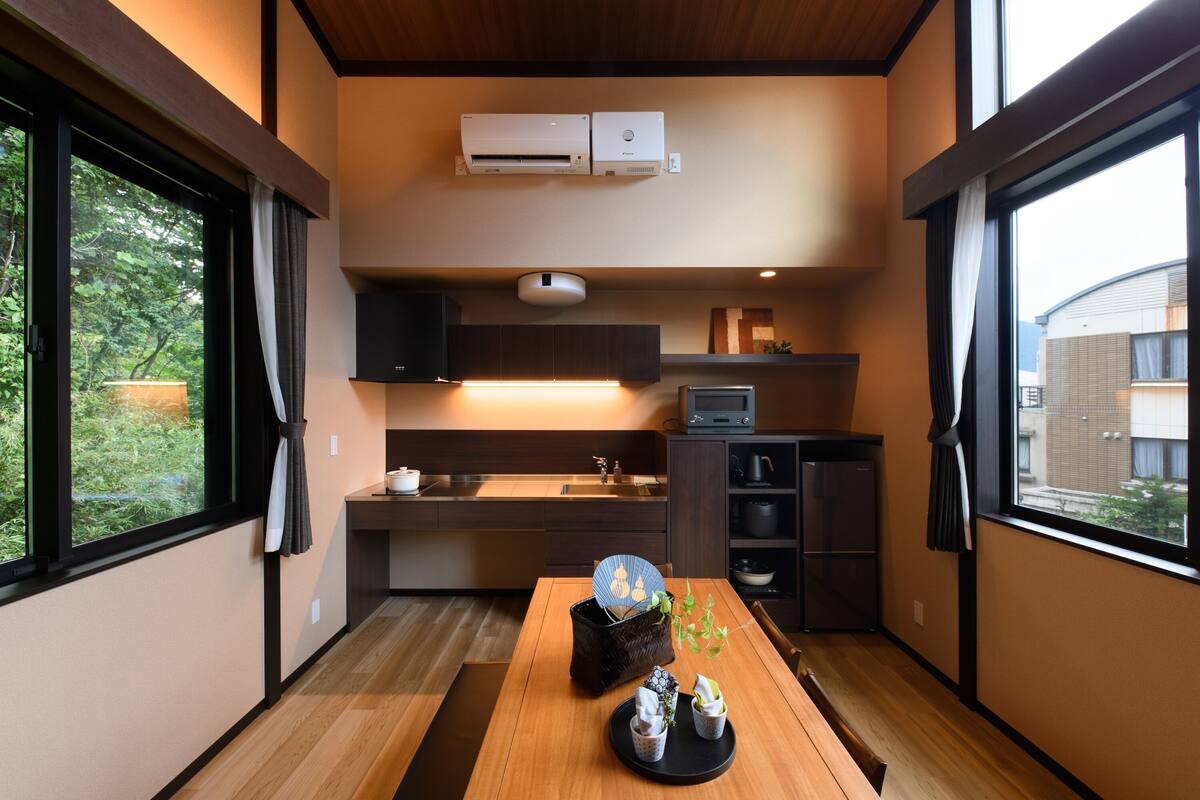 A compact kitchen with a dining area, wooden flooring, and large windows.